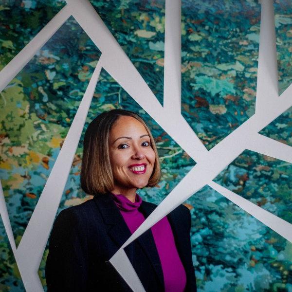 A portrait of Alisha Davis. She is standing in front of a piece of artwork, with it broken apart to look like a mosaic.